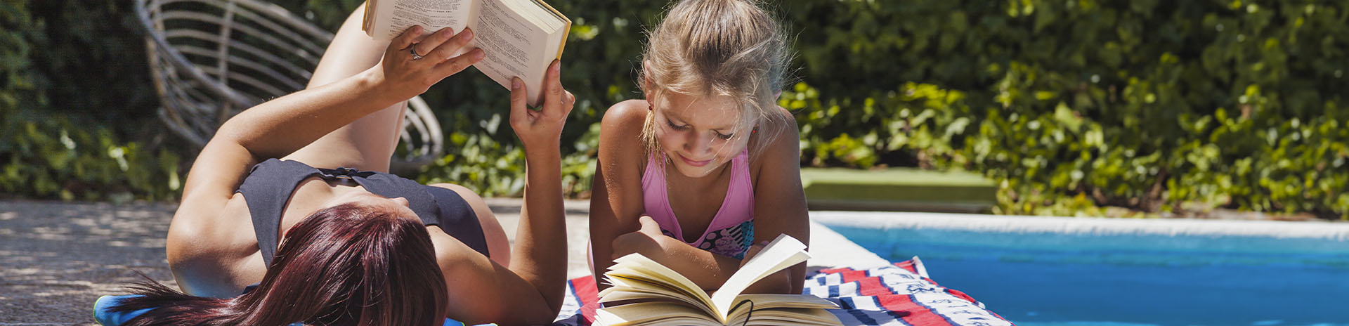 mor og datter ligger og læser i hver deres bog ved en pool en varm sommerdag