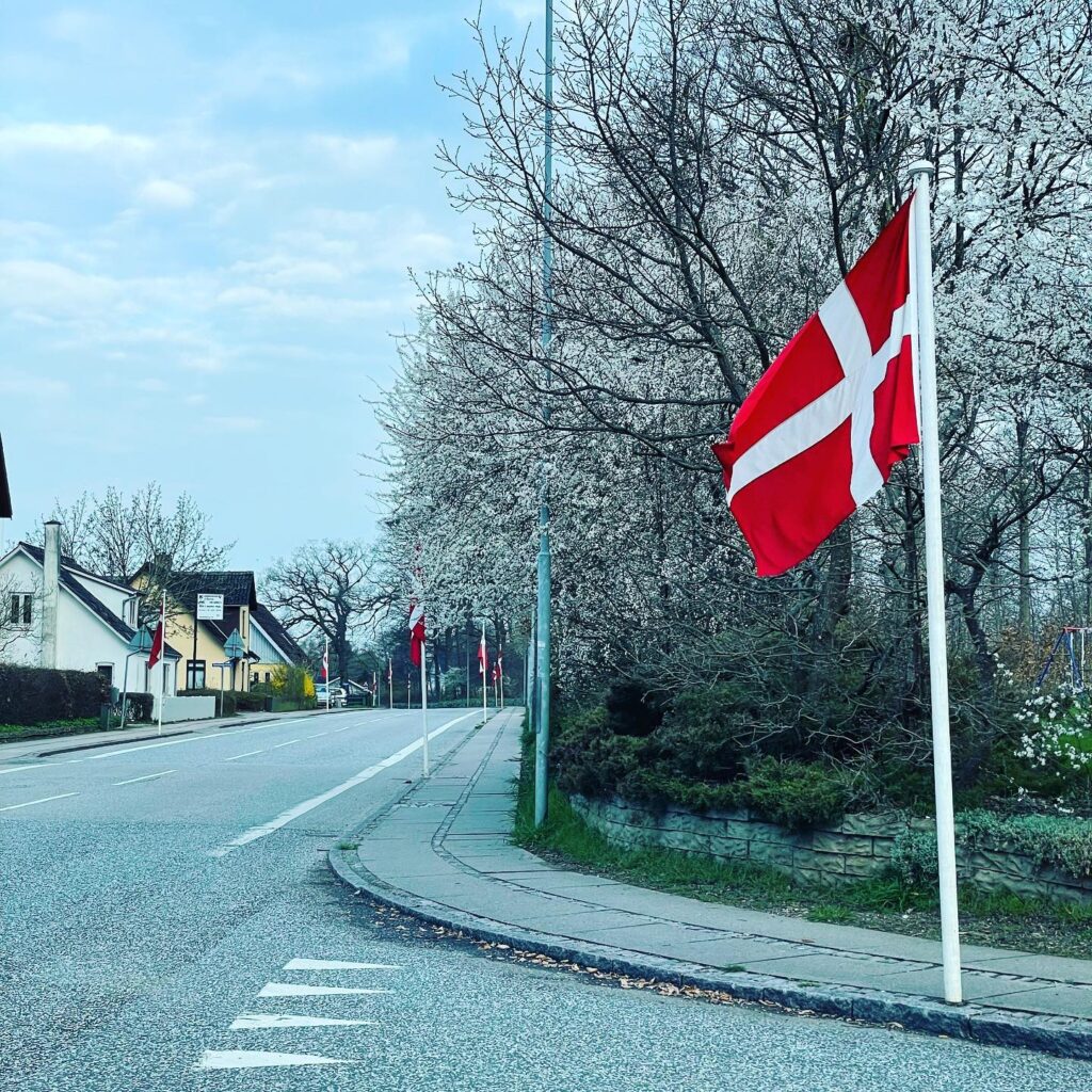 Flagalleens flag vejer smukt i vinden foran træ med udsprungne små hvide blomster den 16. april - Dronningens fødselsdag